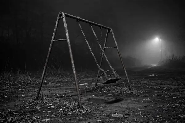 Empty playground at night with swing in fog, black and white creepy wallpaper